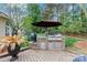 A stone outdoor kitchen area with a built-in grill, lush landscaping, and patio furniture at 1509 Kirkbridge Ct, Matthews, NC 28105