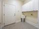 Neutral-toned laundry room features white cabinets, utility sink, tile floor, and exterior door at 16919 Hedgerow Park Rd, Charlotte, NC 28277
