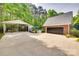 View of the property, with a large driveway, brick garage, carport, and fenced pool area surrounded by lush trees at 2062 High Pines Rd, Rock Hill, SC 29732