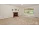 Bright living room featuring a brick fireplace, large windows overlooking the fenced yard, and neutral carpet at 8709 Stratton Farm Rd, Huntersville, NC 28078