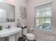 Well-lit half bath with a pedestal sink, modern fixtures, decorative mirror, and a window with natural light at 1607 Tundra Ln, Denver, NC 28037