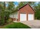 Side view of a brick two-car garage with white doors and light green siding against a backdrop of lush greenery at 2306 Beechwood Dr, Waxhaw, NC 28173