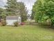 Large grassy backyard, featuring fencing, outbuilding, and mature trees at 2603 Willis Dr, Harrisburg, NC 28075