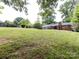 Spacious backyard with a large grassy area, mature trees, and a glimpse of the brick house at 6616 Williams Rd, Charlotte, NC 28215