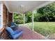 Covered back porch featuring brick floors and walls, two blue chairs, and an open view of the backyard at 6616 Williams Rd, Charlotte, NC 28215