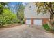 Attached two-car garage with white doors and concrete driveway, surrounded by lush landscaping and mature trees at 2418 Ainsdale Rd, Charlotte, NC 28226