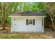 Small white storage shed with covered entry, and black shutters, in a private setting at 7810 Trotter Rd, Charlotte, NC 28216
