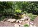 Lush backyard pond featuring rock accents, waterfall feature, mature trees, and wooden fence surrounding a beautiful garden at 5206 Morrowick Rd, Charlotte, NC 28226