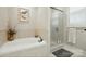 Bright bathroom featuring a corner tub, a frameless glass shower, and neutral-toned tile work with a window above the tub at 9652 Wheatfield Rd, Charlotte, NC 28277