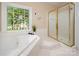 Bright bathroom featuring a garden tub, a glass-enclosed shower, and a large window overlooking lush greenery at 15535 Eagleview Dr, Charlotte, NC 28278
