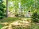 Large backyard with mature trees, green grass and back view of the house with a patio and outdoor umbrella at 166 Wilson Lake Rd, Mooresville, NC 28117