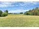 Wide shot of green field, with trees and road in the background under blue sky at 25674 Old School Rd, Oakboro, NC 28129