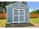 A blue storage shed with white trim, double doors, and a light, located in a grassy backyard at 959 Robinson Rd, Gastonia, NC 28056