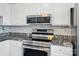 Kitchen boasts stainless appliances, mosaic tile backsplash, white cabinets, and granite counters at 202 Water Oak Dr, Pineville, NC 28134