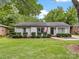 Inviting single-story home showcasing a lush green lawn, classic brick facade, and an American flag by the entrance at 1714 Edgewater Dr, Charlotte, NC 28210