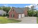 Rear view of a two-story brick home with three-car garage and lush landscaping, partially fenced at 444 Snapdragon Dr, Clover, SC 29710