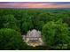Aerial view of a luxurious home surrounded by lush, mature trees and a colorful sky at 5030 Hardison Rd, Charlotte, NC 28226