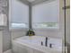 Bright bathroom with a luxurious soaking tub, tiled surround, and natural light from two windows at 15824 Feeny Ct, Charlotte, NC 28278