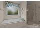 Bathroom featuring a tiled surround deep soaking tub beside a tiled shower with glass doors and a window at 4563 Osprey Run Ct, Denver, NC 28037