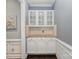 Hallway butler pantry with white cabinets, light stone countertops, and glass-front display cabinets at 10202 Alouette Dr, Waxhaw, NC 28173