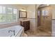 Bright bathroom featuring a soaking tub, glass shower, vanity, and a large window with plantation shutters at 11917 Chevis Ct, Charlotte, NC 28277