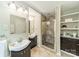 Elegant bathroom featuring double sinks with dark vanities, a tiled shower with a glass door, and linen shelving at 5522 Sharon Rd, Charlotte, NC 28210