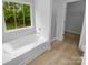 Modern bathroom with a soaking tub beneath a window, complemented by light tile flooring at 2140 Majestic Poplar Dr, Waxhaw, NC 28173