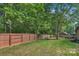 Backyard featuring a wooden fence, deck, green grass, mature trees, and mulch providing a private outdoor space at 2202 Bearskin Ln, Monroe, NC 28110