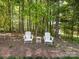 Seating area with two white chairs and a small table situated in a wooded area of the back yard at 10716 Meg Meadow Dr, Mint Hill, NC 28227