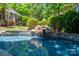 Tranquil swimming pool with a natural rock waterfall feature surrounded by lush greenery and landscaping at 8028 Water View Dr, Belmont, NC 28012