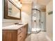 Bright bathroom with a glass shower, wood vanity, decorative mirror, and neutral colored tile flooring at 8239 Victoria Lake Dr, Waxhaw, NC 28173