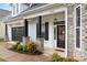 Inviting front porch with stone pillars, black door, manicured landscaping, and a brick and stone facade at 14119 Shelburne Village Dr, Charlotte, NC 28278
