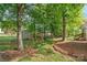 Backyard showing mature trees, green grass, and a wooden playset. A wonderful space to enjoy the outdoors at 1542 Crowders Woods Dr, Gastonia, NC 28052