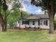 Quaint exterior of a home with a covered porch and black shutters, framed by mature trees in a green yard at 4630 Roberta Rd, Concord, NC 28027
