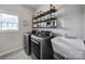 Functional laundry room features modern washer and dryer, rustic shelving, a wash basin, and tiled floors at 2218 Legacy Oak Dr, Waxhaw, NC 28173