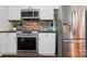 Kitchen with stainless steel appliances including microwave and stove, white cabinets, and mosaic backsplash at 4132 Kenton Glenn Nw Ct, Concord, NC 28027