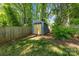 Backyard storage shed with double doors, sitting on a grassy lawn and surrounded by tall trees and a wooden fence at 2933 Hilliard Dr, Charlotte, NC 28205