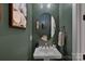 Stylish powder room with a round mirror, white sink, and green accent wall with flower art at 7730 Burning Ridge Dr, Stanley, NC 28164