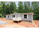 New single-story home with gray siding, a small porch, and surrounded by trees and earth in an undeveloped lot at 1785 Doe Ct, Iron Station, NC 28080