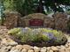 Stone sign for Olde Sycamore Swim & Racquet Club surrounded by colorful flowers and river rock, showcasing a welcoming entrance at 10944 Persimmon Creek Dr, Mint Hill, NC 28227
