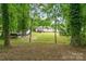 The backyard features large trees, a green lawn and the back of the house with a wooden deck at 195 Kings Ter, Salisbury, NC 28146