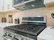 Close-up of a modern stainless steel gas range with white countertops, tiled backsplash, and stylish overhead microwave at 5219 Farmbrook Dr, Charlotte, NC 28210