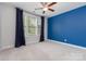 Cozy bedroom featuring a bold blue accent wall, ceiling fan and window with dark curtains at 8210 Festival Way, Charlotte, NC 28215