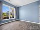 Simple bedroom with blue walls, hardwood floors, a large window with gray curtains, and white trim at 11931 The Ramble Dr, Huntersville, NC 28078