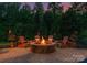 Cozy outdoor stone fire pit with Adirondack chairs, surrounded by lush greenery and landscape lighting at 1021 Westbury Dr, Matthews, NC 28104