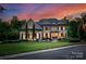 Imposing brick home with black shutters, manicured lawn, mature trees and twilight sky at 1021 Westbury Dr, Matthews, NC 28104