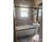 Well-lit bathroom features tub with glass door, decorative window, neutral tile and a pedestal sink at 1658 Hillcrest Ave, Lancaster, SC 29720