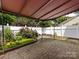 Covered back patio with brick pavers and a white fence adorned with lovely flowers and manicured bushes at 2502 Breuster Dr, Charlotte, NC 28210