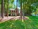 View of a two story house with neutral siding, black shutters, and green lawn surrounded by mature shade trees at 2600 Kirkholm Dr, Matthews, NC 28105
