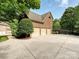 Three car garage, brick facade, and paved driveway framed by mature trees and shrubbery at 16319 Ashlyn Chase Ct, Charlotte, NC 28277
